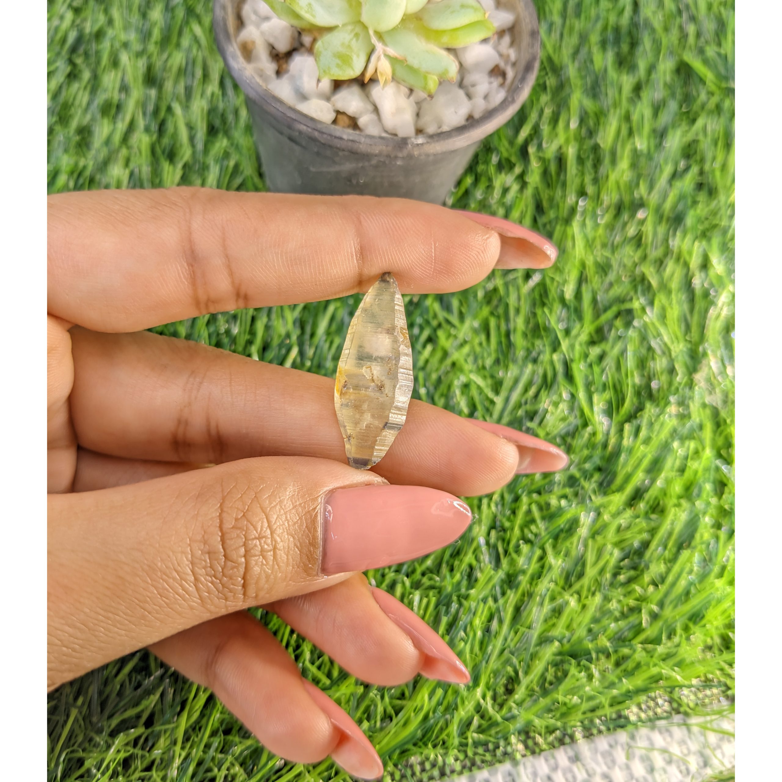 Natural rough yellow sapphire crystal held between fingers above a green lawn mat